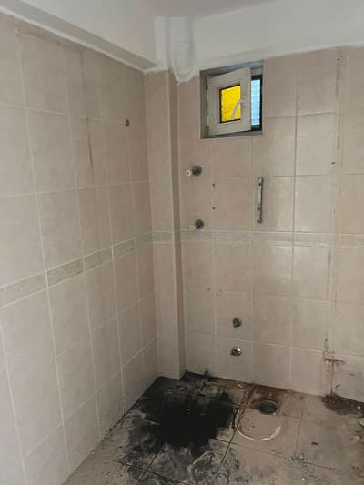 Eski banyo: krem fayans, göbek hizasında desenli bordür. Klozet sökülmüş, yerinde izi ve yer süzgeci duruyor.